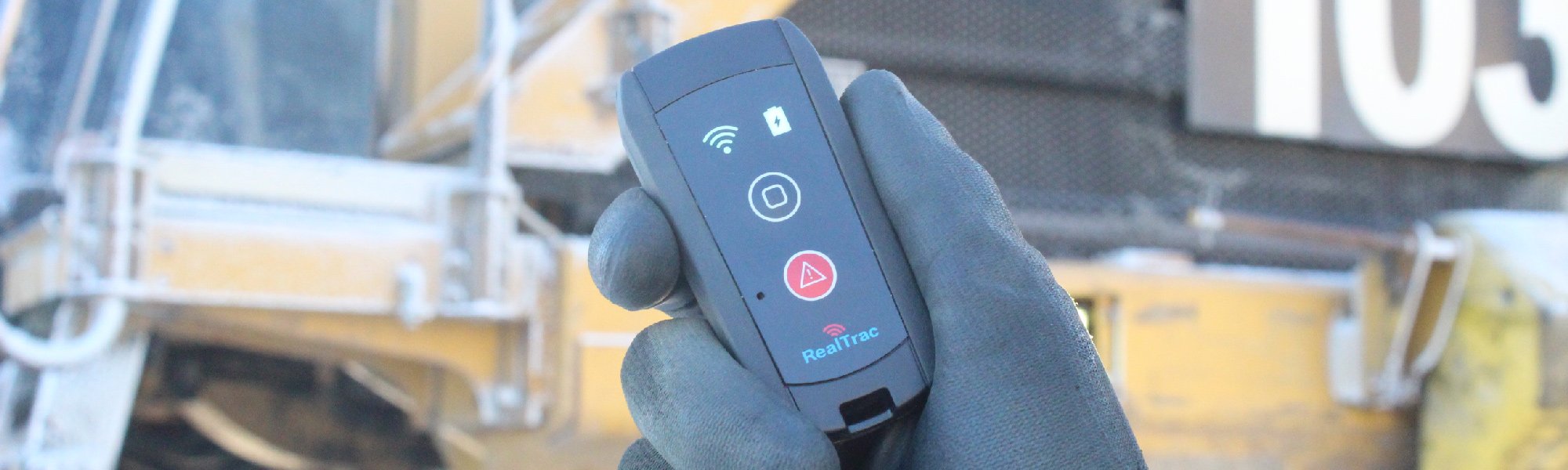 RealTrac PROD TAG 210 personal tag in a worker's hand against a mining haul truck